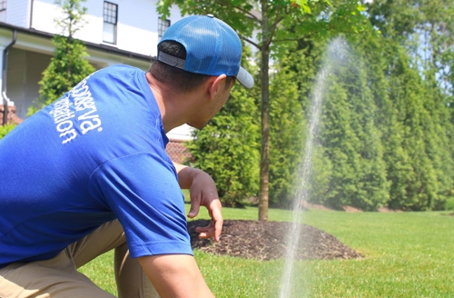 Sprinkler man kneeling down and adjusting sprinkler.