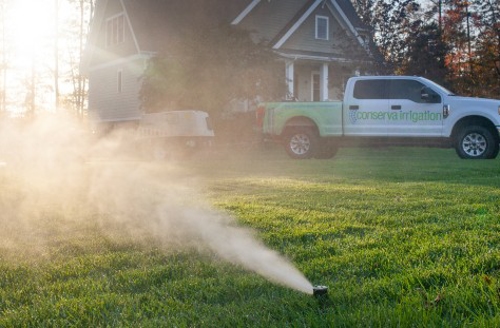 house and truck in background of sprinkling spraying grass