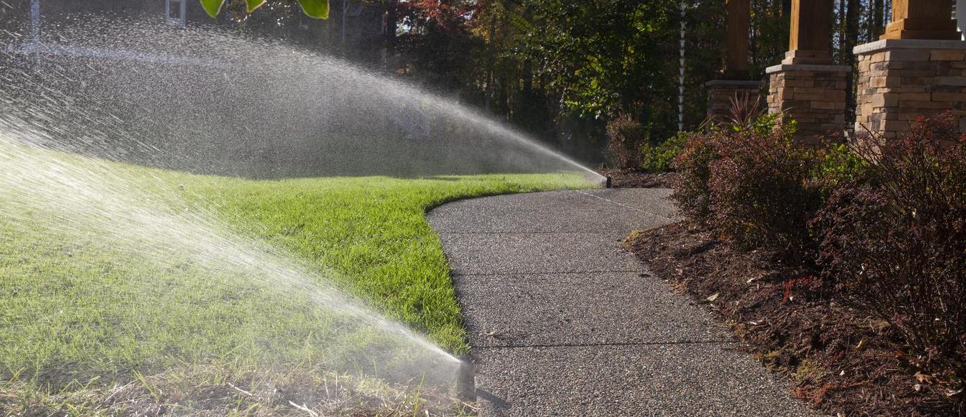 Two sprinklers spraying water on a grass lawn next to a pathway