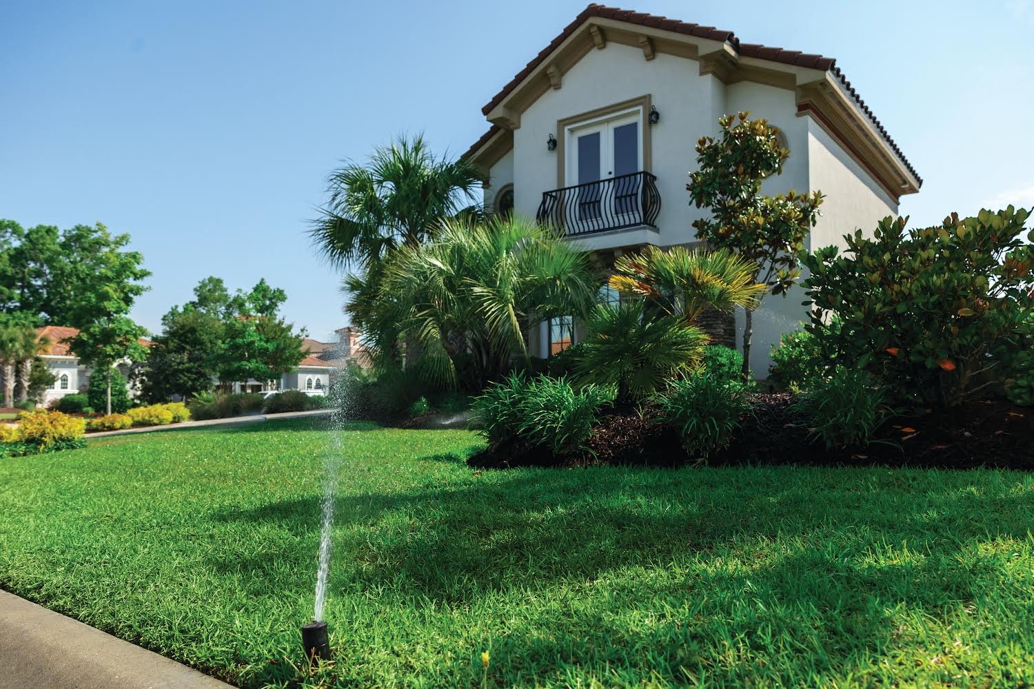 sprinklers in front yard with a house in the background